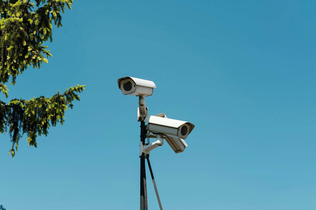 Two white security cameras mounted on a pole against a clear blue sky
